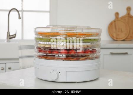 Entwässerungsmaschine mit verschiedenen Früchten und Beeren auf einem weißen Tisch in der Küche Stockfoto