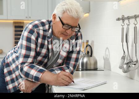 Senior-Mann löst Sudoku-Rätsel an der Küchentheke Stockfoto