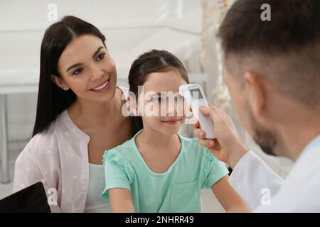 Mutter mit Tochter beim Kinderarzt im Krankenhaus. Doktor misst die Temperatur eines kleinen Mädchens Stockfoto