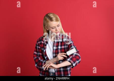 Junge Frau putzt Kleidung mit Fusselrolle auf rotem Hintergrund Stockfoto