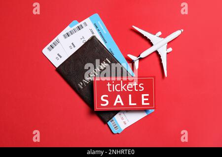 Flugtickets, Reisepass, Flugmodell und VERKAUFSKARTE auf rotem Hintergrund, flach liegend Stockfoto