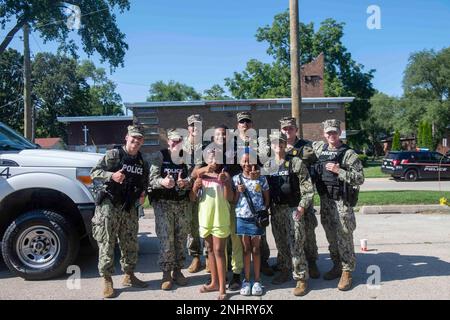 NORTH CHICAGO Il. (2. August 2022) Matrosen, die der Naval Station Great Lakes zugeteilt sind, posieren für ein Gruppenfoto mit einer Familie während der National Night in North Chicago. National Night Out ist eine jährliche Kampagne zum Aufbau von Gemeinwesen, die Partnerschaften zwischen Polizei und Gemeinwesen und Nachbarschaftskameradschaft fördert. National Night Out verbessert die Beziehung zwischen Nachbarn und Strafverfolgungsbehörden und bringt gleichzeitig ein echtes Gemeinschaftsgefühl zurück. Stockfoto