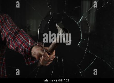 Ein Mann zertrümmert Fenster mit Hammer auf schwarzem Hintergrund, schließt auf Stockfoto