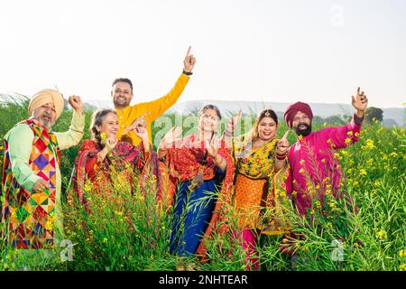 Die Familie Punjabi sikh tanzt Bhangra auf dem Landwirtschaftsfeld und feiert das Baisakhi- oder Vaisakhi-Festival. Stockfoto