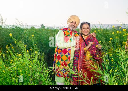 Portrait eines glücklichen Senior-Punjabi-sikh-Paares, das bunte Tücher trug, die auf dem Landwirtschaftsfeld zusammenstanden. Ich schaue in die Kamera. Stockfoto