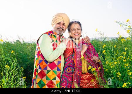 Portrait eines glücklichen Senior-Punjabi-sikh-Paares, das bunte Tücher trug, die auf dem Landwirtschaftsfeld zusammenstanden. Ich schaue in die Kamera. Stockfoto