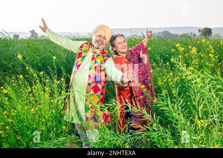 Fröhliches Senior-Punjabi-sikh-Paar, das Bhangra-Tanz auf dem Landwirtschaftsfeld veranstaltet und das Baisakhi- oder Vaisakhi-Festival feiert. Stockfoto