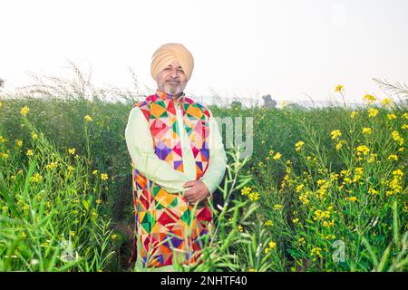 Portrait von Happy Senior Punjabi sikh Mann in heidnischem und farbenfrohem, traditionellem Outfit, der auf dem Landwirtschaftsfeld steht. Stockfoto