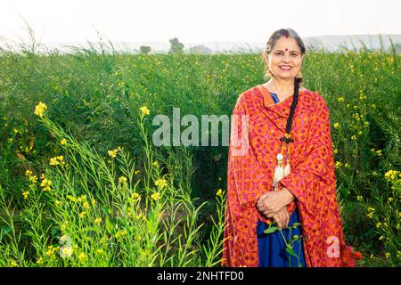 Porträt einer Happy Senior Punjabi Frau in bunten, traditionellen Outfits, die auf dem Landwirtschaftsfeld steht. Stockfoto