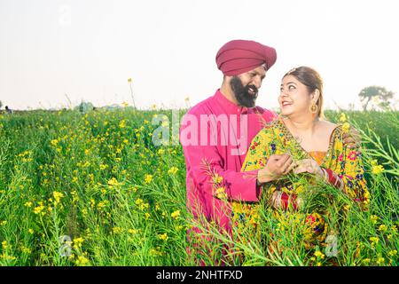 Glückliches junges Punjabi-sikh-Paar, das auf dem Landwirtschaftsfeld zusammensteht. Beide sehen sich mit einem Lächeln an. Stockfoto