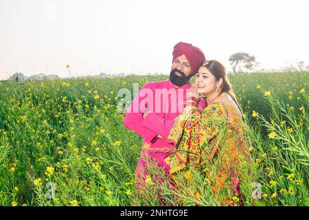 Glückliches junges Punjabi-sikh-Paar, das auf dem Landwirtschaftsfeld zusammensteht. Stockfoto