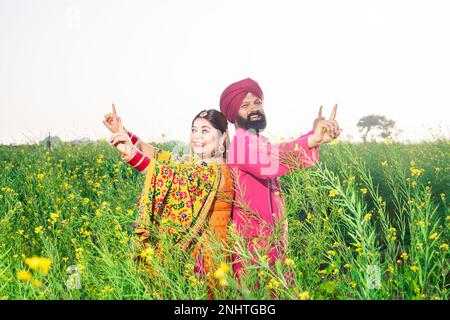 Glückliches Punjabi-sikh-Paar, das Bhangra-Tanz auf dem Landwirtschaftsfeld veranstaltet und das Baisakhi- oder Vaisakhi-Festival feiert. Stockfoto