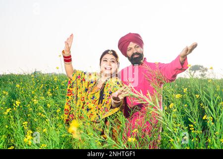 Fröhliches Punjabi-sikh-Paar, das Bhangra-Tanz auf dem Landwirtschaftsfeld veranstaltet und das Baisakhi- oder Vaisakhi-Festival feiert. Stockfoto