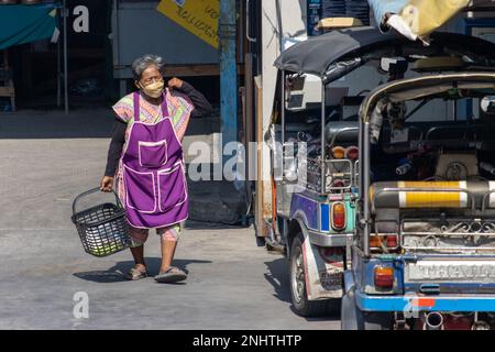 SAMUT PRAKAN, THAILAND, FEBRUAR 13 2023, eine ältere Frau in einer Schürze fährt in ein motorisiertes, dreirädriges Tuk Tuk Taxi Stockfoto