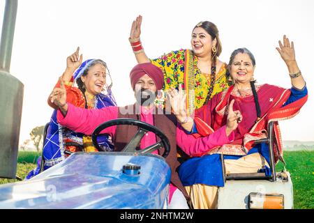 Happy punjabi sikh Farmer Family sitzt auf Traktortanz und feiert draußen. Wohlstandskonzept. Stockfoto