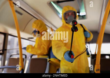 Öffentliche Verkehrsmittel Sanitäreinrichtungen. Arbeiter in Schutzanzügen desinfizieren Bussalon, Fokus auf Spritzmaschinendüse Stockfoto