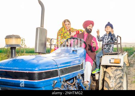 Glückliche junge bauernfamilie aus punjab, die auf Traktortänzen sitzt und draußen feiert. Ländliches indien und Wohlstandskonzept. Stockfoto