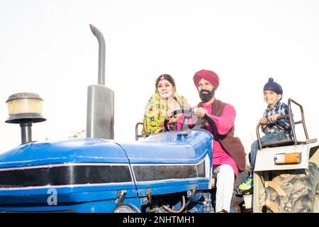 Glücklicher bauer in punjab sikh, der den Traktor im Freien mit seiner Frau und seinem Kind fährt. Ländliches indien. Stockfoto