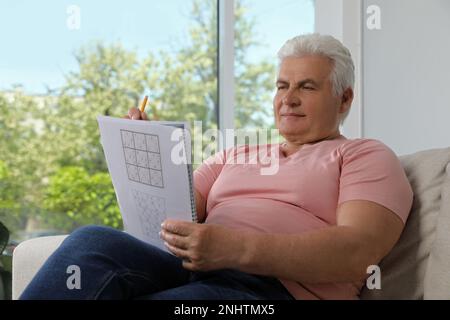 Senior-Mann löst Sudoku-Rätsel auf dem Sofa zu Hause Stockfoto