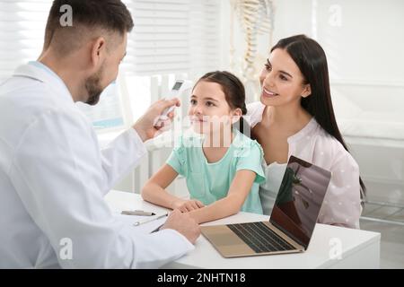 Mutter mit Tochter beim Kinderarzt im Krankenhaus. Doktor misst die Temperatur eines kleinen Mädchens Stockfoto