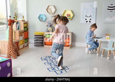 Süße kleine Mädchen, die zu Hause Hopscotch spielen Stockfoto