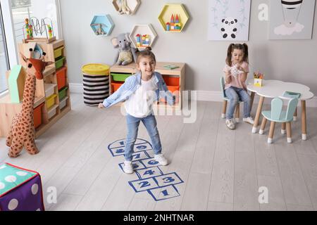 Süße kleine Mädchen, die zu Hause Hopscotch spielen Stockfoto