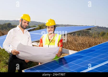 Junge indische Techniker stehen und planen die Installation von Solarpaneelen. Industriearbeiter diskutieren über die Installation von Solarsystemen, alt Stockfoto