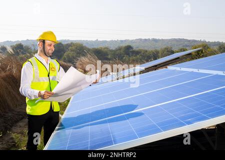 Porträt eines jungen indischen Technikers, der einen gelben Schutzhelm trägt und Solarpaneele installieren will. Industriebetrieb, der Solaranlagen installiert Stockfoto