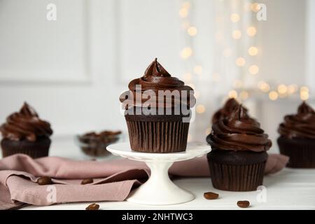 Köstliche Schokoladen-Cupcakes mit Sahne auf einem weißen Tisch vor verschwommenem Licht Stockfoto