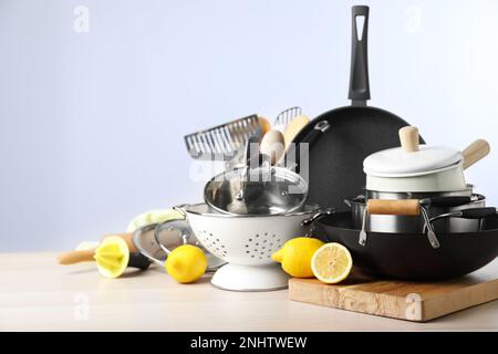 Set aus sauberem Küchengeschirr und Zitronen auf Holztisch vor hellem Hintergrund. Platz für Text Stockfoto