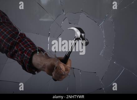 Ein Mann zertrümmert Fenster mit Hammer auf grauem Hintergrund, Nahaufnahme Stockfoto