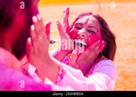 Glückliches, junges indisches Paar, das Spaß beim Spielen mit bunten Pulverfarben hat, oder Gulal beim holi Festival im Park Outdoor. Nahaufnahme. Stockfoto