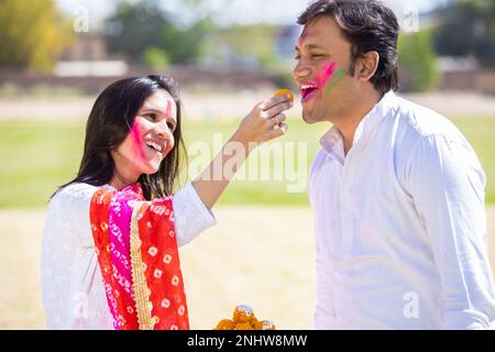 Glückliches junges indisches Paar, das das holi Festival zusammen feiert und dabei köstlichen Laddu Sweet genießt. Stockfoto