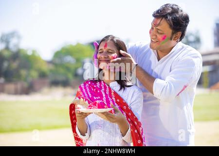 Ein glückliches, junges indianisches Paar, das weiße Kurta trägt und im Park zusammen holi feiert. Stockfoto