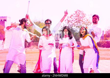 Eine Gruppe fröhlicher junger Indianer, die das holi Festival im Park im Freien feiern und Spaß miteinander haben, verspielter erwachsener Mann und Freunde mit bunten Schmerzen Stockfoto