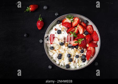 Hüttenkäse, Quark mit frischen Erdbeeren, Heidelbeeren, Nüssen und Joghurt in einer Schüssel. Gesundes Milchprodukt reich an Kalzium und Protein. Obere V-Achse Stockfoto