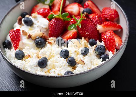 Hüttenkäse, Quark mit frischen Erdbeeren, Heidelbeeren, Nüssen und Joghurt in einer Schüssel. Gesundes Milchprodukt reich an Kalzium und Protein. Stockfoto