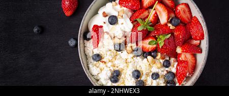 Hüttenkäse, Quark mit frischen Erdbeeren, Heidelbeeren, Nüssen und Joghurt in einer Schüssel. Gesundes Milchprodukt reich an Kalzium und Protein. Obere V-Achse Stockfoto