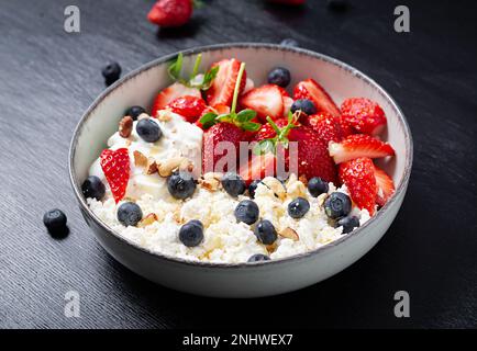 Hüttenkäse, Quark mit frischen Erdbeeren, Heidelbeeren, Nüssen und Joghurt in einer Schüssel. Gesundes Milchprodukt reich an Kalzium und Protein. Stockfoto