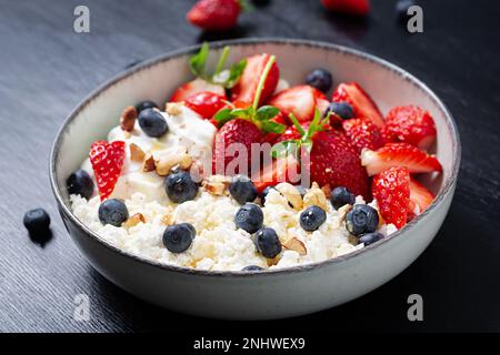 Hüttenkäse, Quark mit frischen Erdbeeren, Heidelbeeren, Nüssen und Joghurt in einer Schüssel. Gesundes Milchprodukt reich an Kalzium und Protein. Stockfoto