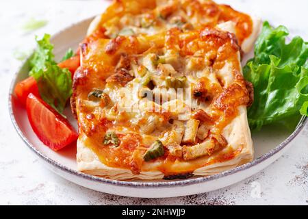 Kleine Kinderpizza, kleine offene Kuchen mit Schinken, Tomatensoße, Mozzarella und Käse im Korb auf hellem Hintergrund. Stockfoto
