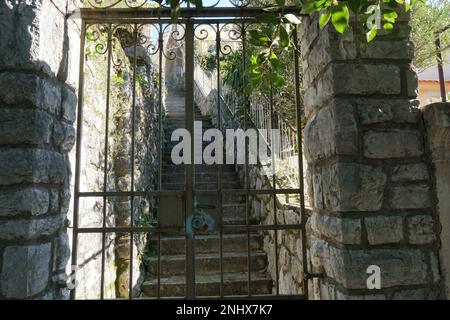 Altes Eingangstor oder Tor aus Metall mit Türschloss, das zu steilen Treppen führt. Die Pfosten bestehen aus gleichmäßigen weißen Steinen. Stockfoto