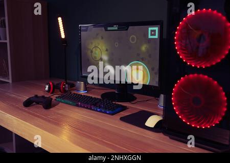 Moderner Computer und RGB-Tastatur auf Holztisch im Zimmer Stockfoto