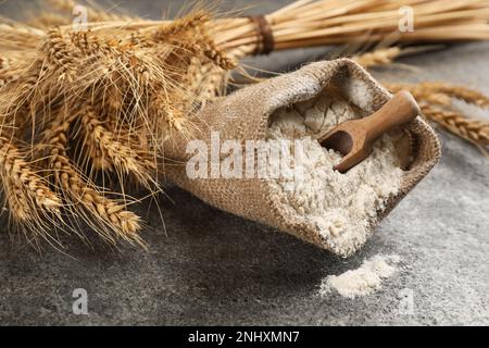 Mehlsack mit Holzschaufel und Weizenohren auf grauem Tisch Stockfoto