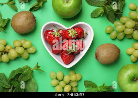 Frische reife Erdbeeren, Äpfel, Trauben, Kiwis und Minze auf grünem Hintergrund, flach gelegen Stockfoto