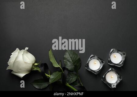 Rose mit schwarzem Band und Kerzen auf dunklem Hintergrund, flach liegend. Platz für Text Stockfoto