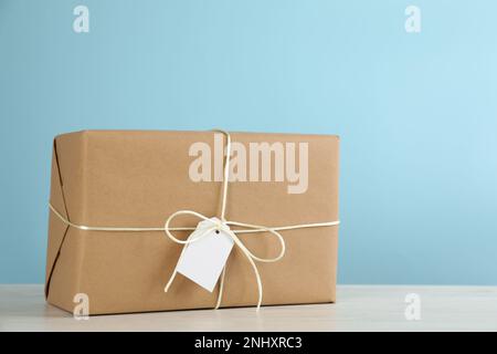 Paket in Kraftpapier eingewickelt mit Anhänger auf weißem Holztisch auf hellblauem Hintergrund Stockfoto