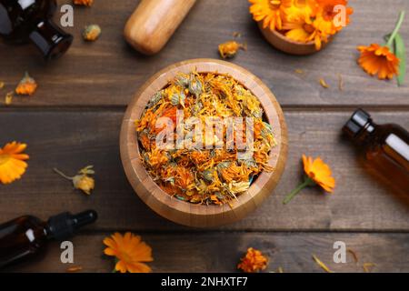 Trockene Kalendelblumen und Flaschen ätherischen Öls auf Holztisch, flach liegend Stockfoto