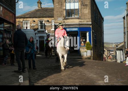 Haworth, West Yorkshire, Großbritannien. Pferde durch Haworth reiten. Haworth ist ein beliebtes Dorf, das berühmt ist als Heimat der Bronte Sisters Stockfoto