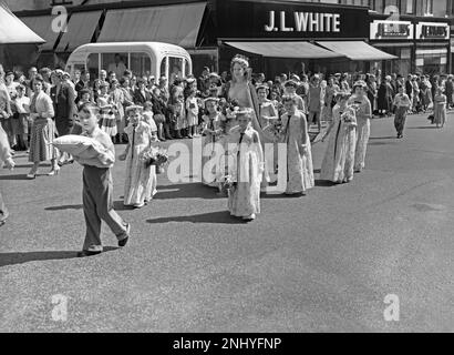 Eine Whit Walks-Prozession in Union Street, Oldham, Greater Manchester, Lancashire, England, UK c.1960. Eine „Rose Queen“ trägt ihre Krone und ist von Kindern umgeben, die Blumen tragen. Im Hintergrund befindet sich ein O'Donnell's Eiswagen. Die religiöse Veranstaltung in der Church of England fand traditionell am Whit Friday statt, an dem Kinder zusammen mit Messingbändern und Silberbändern beteiligt waren. Dieses Foto stammt aus einem alten Schwarz-Weiß-Negativ – einem klassischen 1950er/60s-Foto. Stockfoto